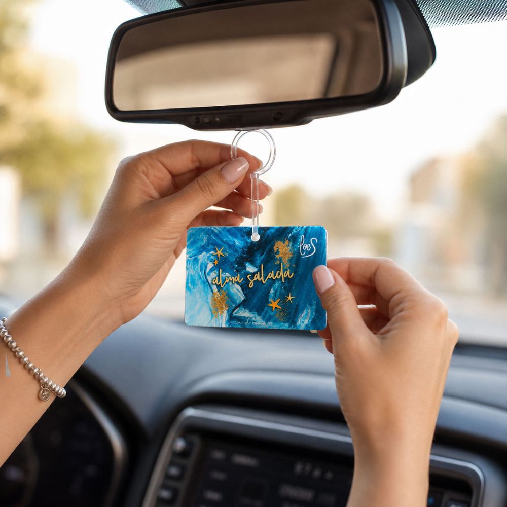 Detalle de unas manos colocando el ambientador de coche Alma Salada de LoeS colgando del espejo retrovisor en el interior de un vehículo – D'Arome