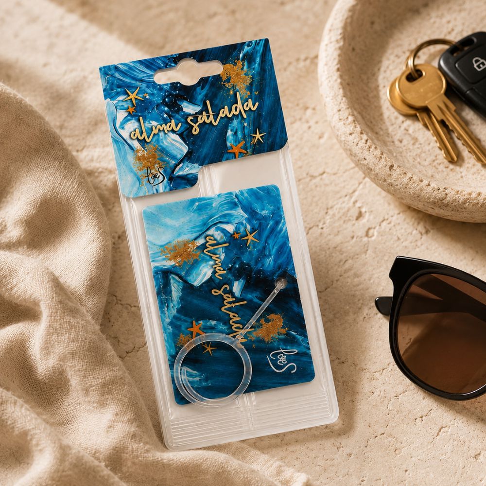 Ambientador de coche Alma Salada de LoeS en su packaging blister junto a las llaves del coche y unas gafas de sol sobre lino natural – D'Arome