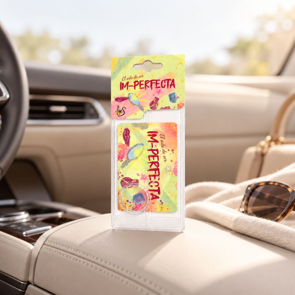 Ambientador de coche Im-Perfecta de LoeS apoyado en la consola central, junto a unas gafas de sol y un bolso de viaje – D'Arome
