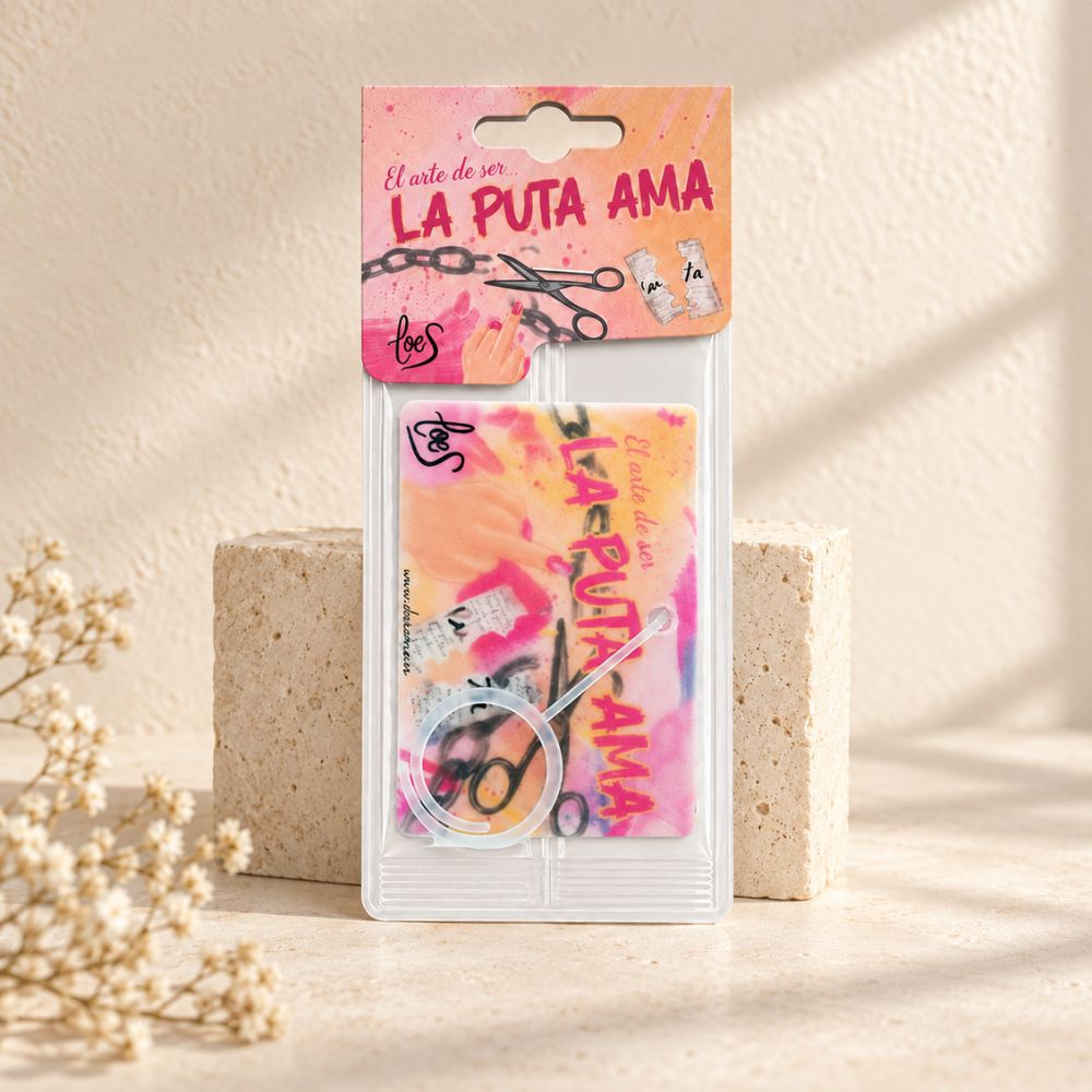 Ambientador de coche La Puta Ama LoeS en su blister sobre superficie de piedra clara con flores secas – D'Arome