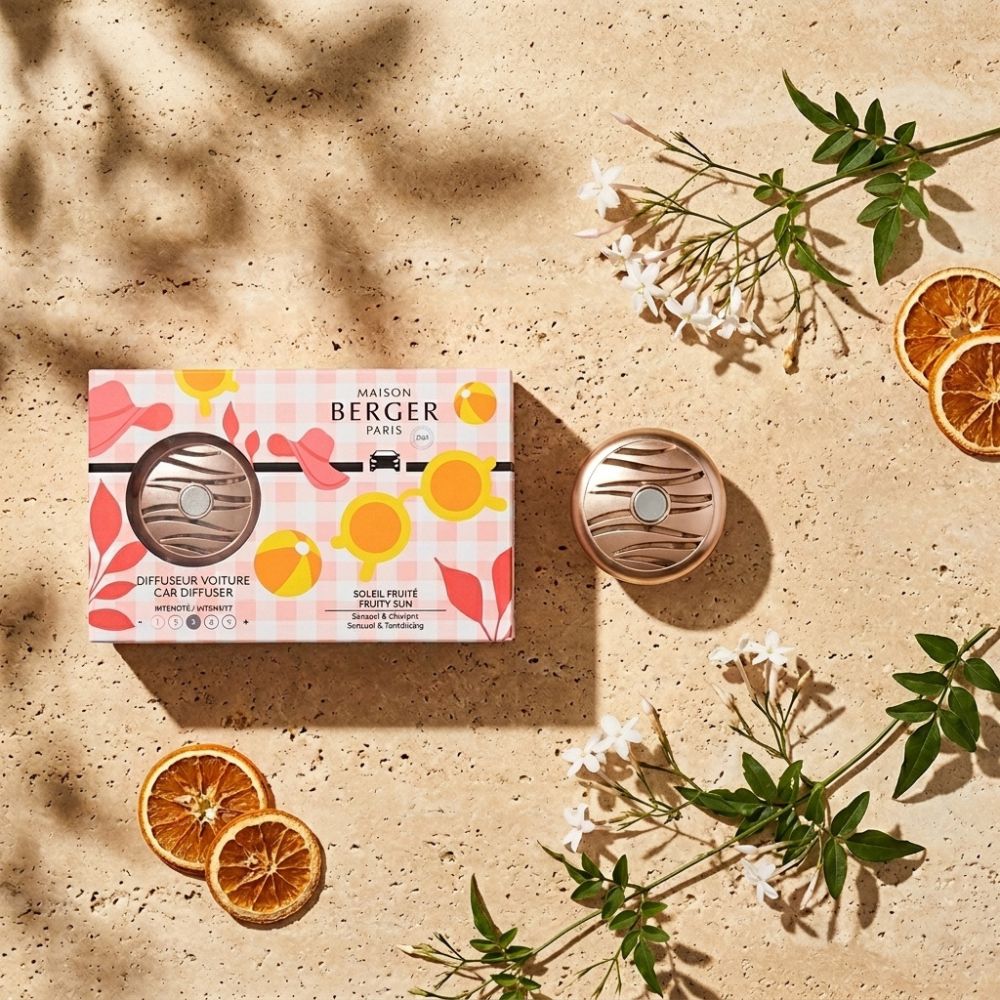 Caja colección Estivale ambientador de coche Soleil Fruité Maison Berger sobre piedra natural con flores blancas y naranja seca – D'Arome