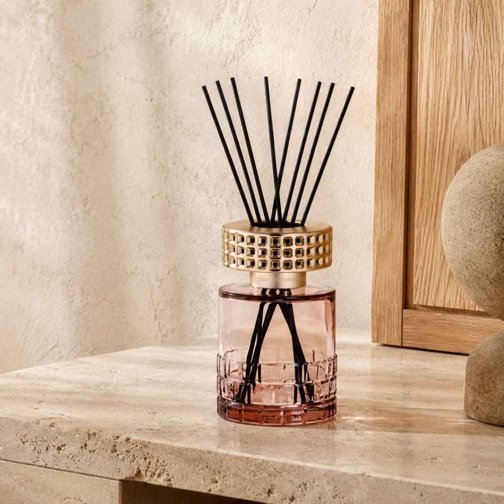 Ambientador Mikado Celebration de Maison Berger en cristal rosa con capuchón dorado calado y varillas negras sobre piedra natural – D'Arome