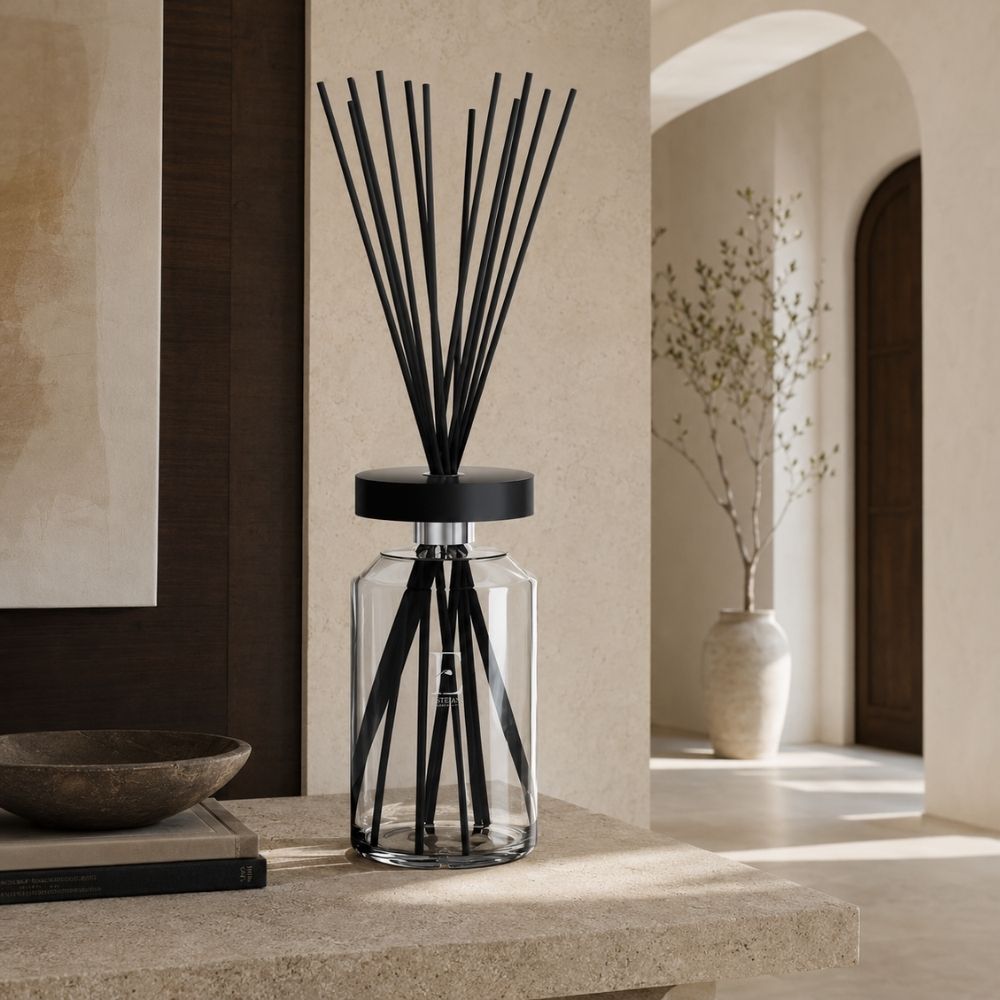 Difusor mikado Ellipse Édition Premium Figue Noire de Esteban Paris, varillas negras en forma de abanico sobre banco de piedra junto a un olivo – D'Arome