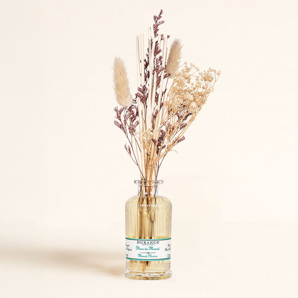 Frasco de vidrio del ambientador mikado Flor de Monoï de Durance en detalle, con su ramo de flores secas naturales y varillas de ratán.