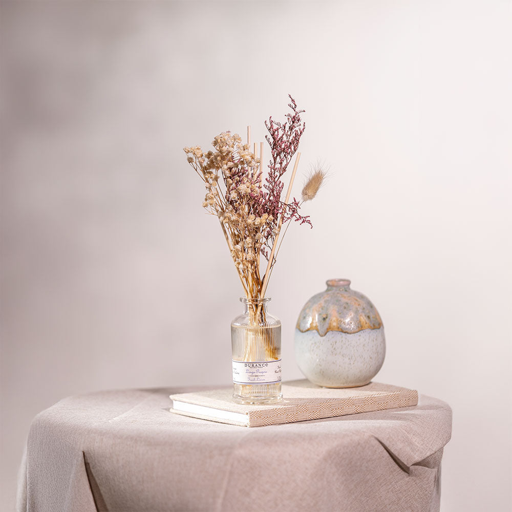Difusor de aromas Ropa Limpia de Durance con ramo de flores secas en un rincón acogedor, aportando un toque natural y elegante sobre un libro.