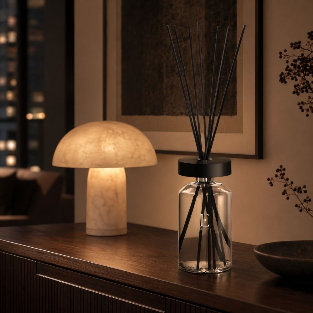 Difusor mikado Ellipse Figue Noire de Esteban Paris sobre aparador de madera oscura, iluminado junto a una lámpara de mármol tipo seta – D'Arome