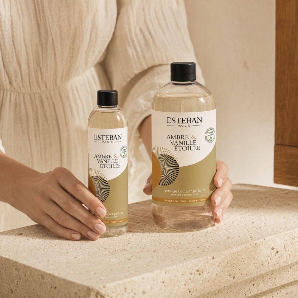 Manos de mujer mostrando comparativa de tamaños del recambio ambientador mikado Ambre et Vanille Étoilée Esteban París en formato 250 ml y 500 ml – D'Arome