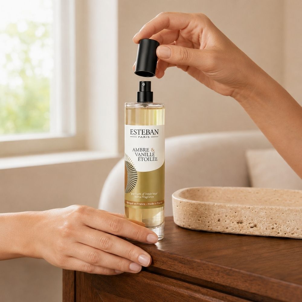 Detalle de manos abriendo el ambientador spray Ambre et Vanille Étoilée Esteban París sobre mueble de madera – D'Arome