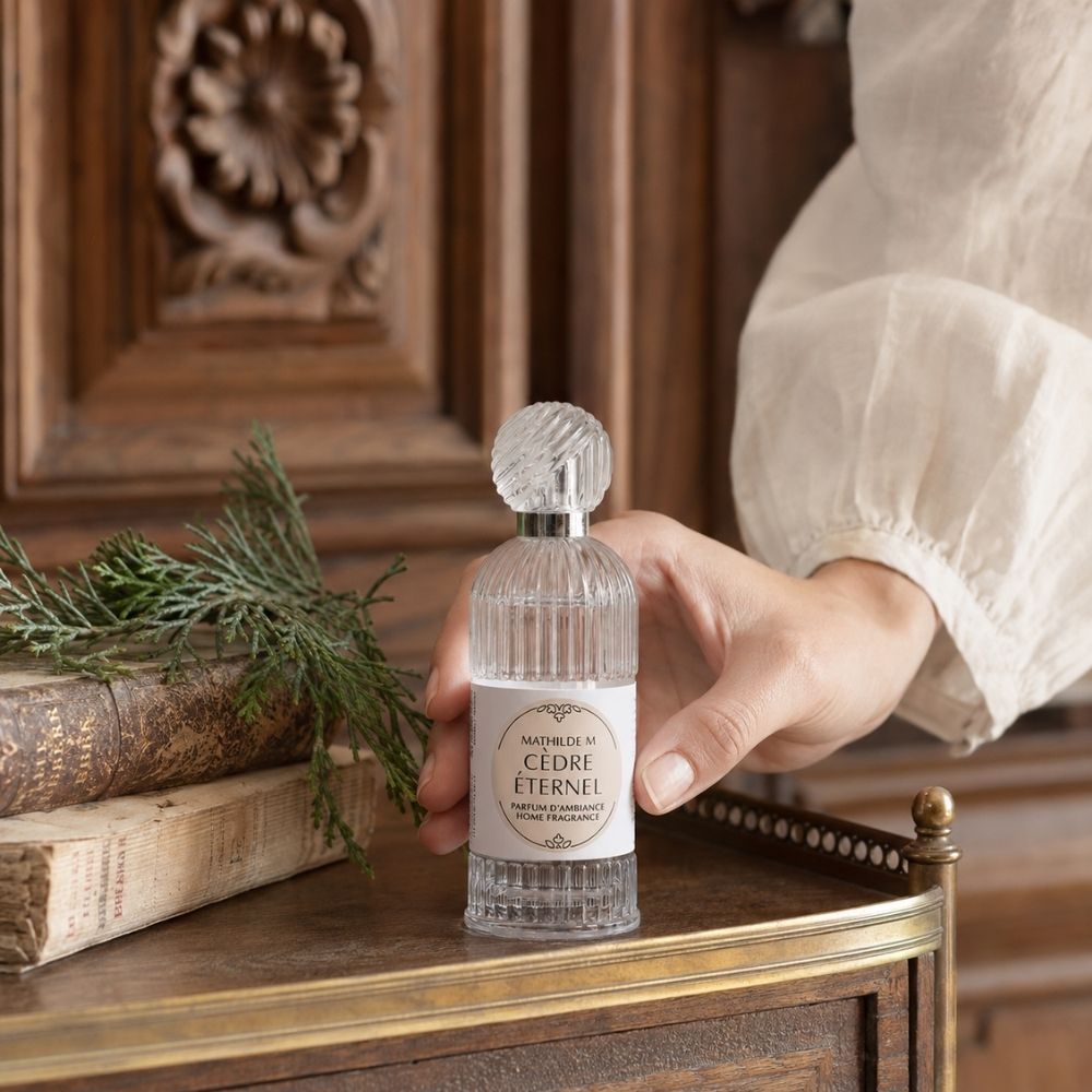 Persona sujetando el ambientador spray Cèdre Éternel Mathilde M sobre cómoda de madera tallada – D'Arome