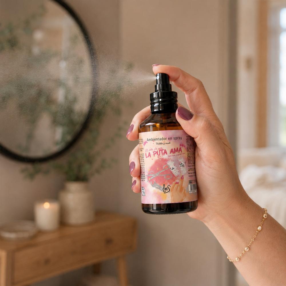 Mano con uñas moradas aplicando spray La Puta Ama LoeS violeta y musk con bruma visible frente a espejo redondo, ambientador perfumador de hogar – D'Arome