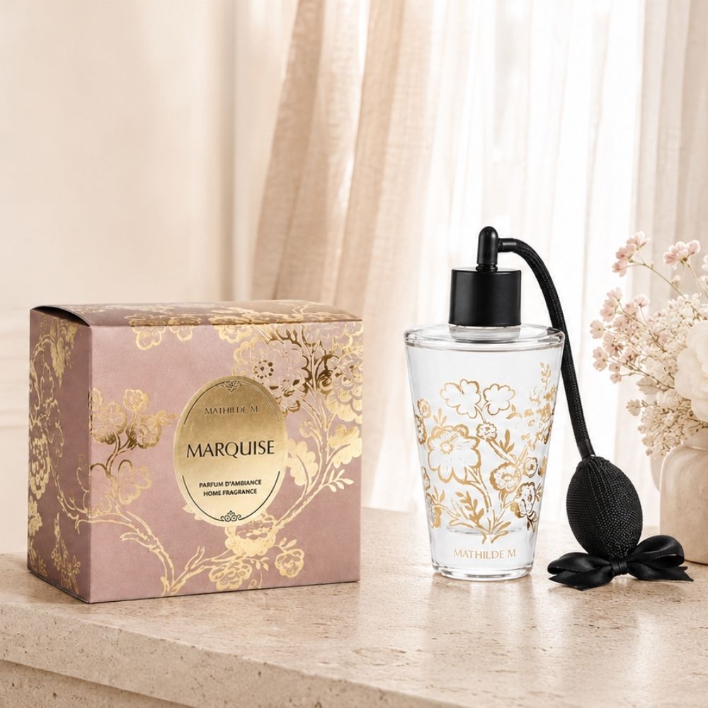 Ambientador spray Trésor de Fleurs con el aroma icónico Marquise de Mathilde M sobre repisa de mármol con su caja de regalo y flores rosas de fondo – D'Arome