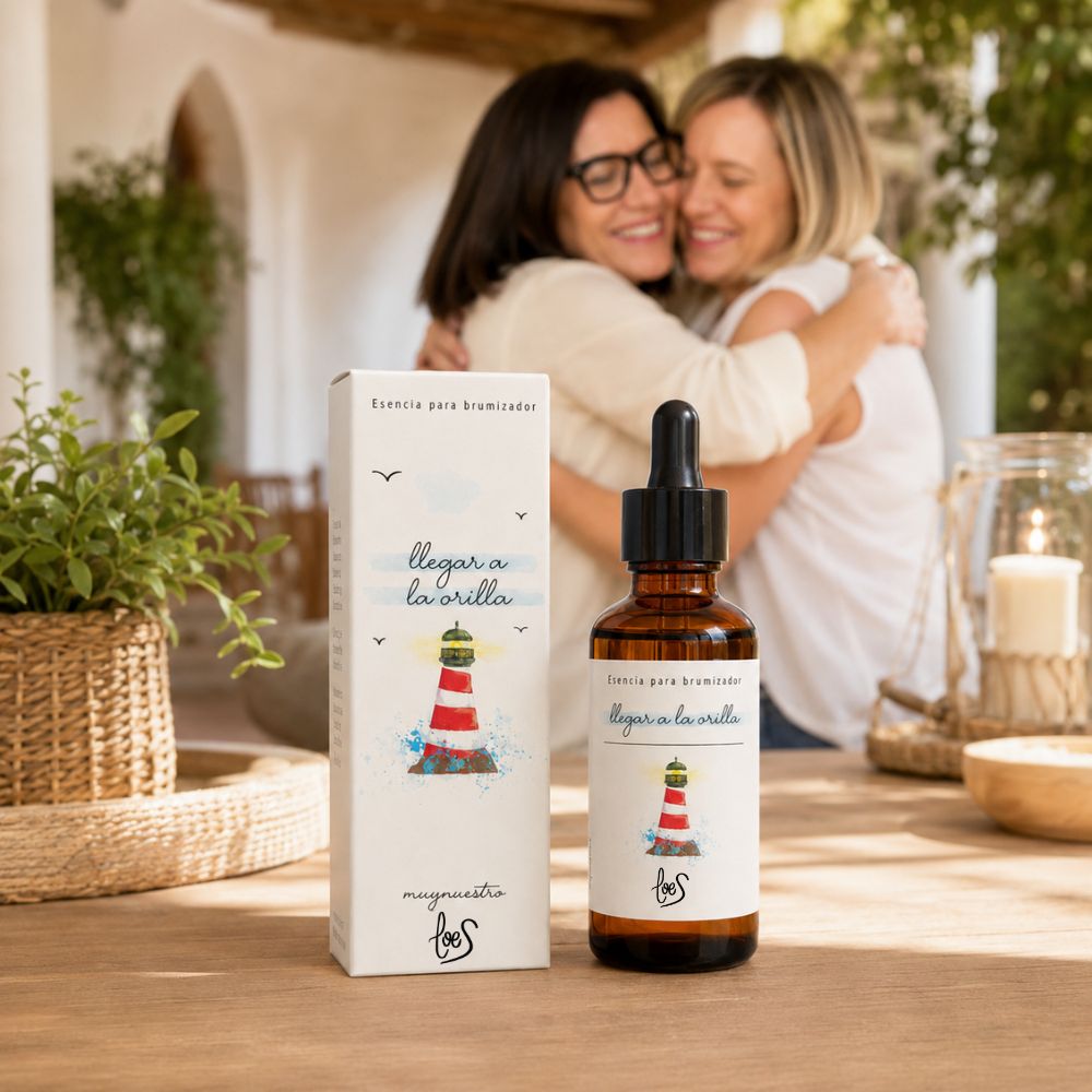 Dos amigas abrazadas en el reencuentro con la esencia para difusor de aromas "Llegar a la orilla" de LoeS en primer plano, ambiente cálido mediterráneo – D'Arome