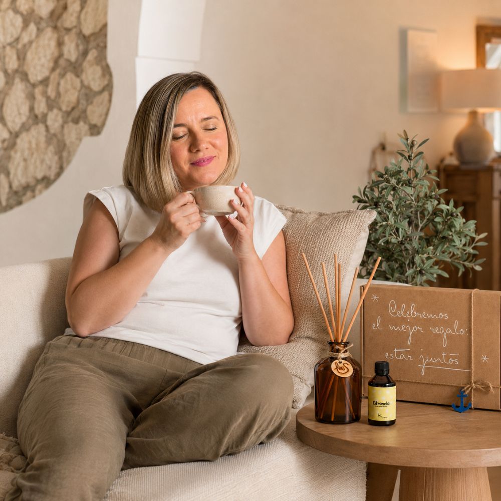 Ana Belén, del equipo de D'Arome, disfrutando de un café en el sofá junto al frasco mikado Citronela de LoeS y el cofre regalo de verano, ambiente hogar relajado – D'Arome