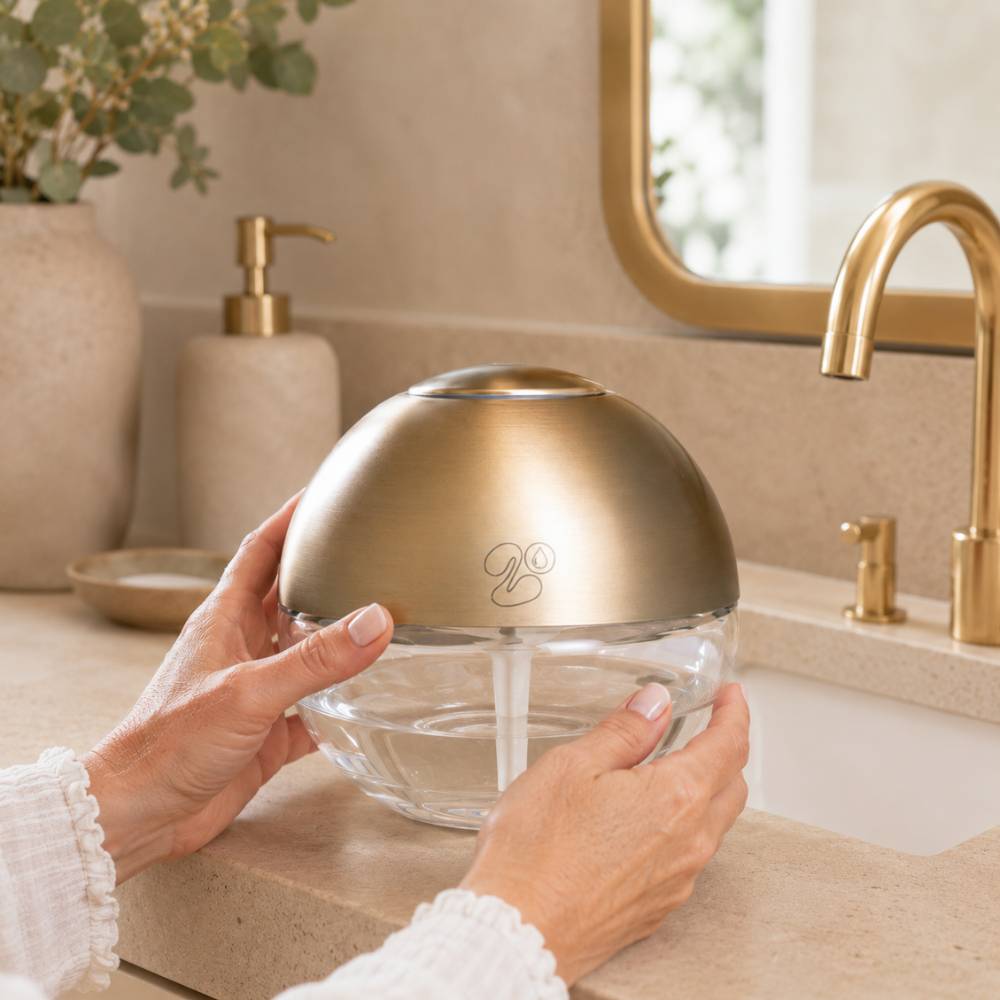 Manos sujetando la bola de olor grande LoeS dorada en baño, brumizador eléctrico 600ml que lava el aire y perfuma el hogar – D'Arome
