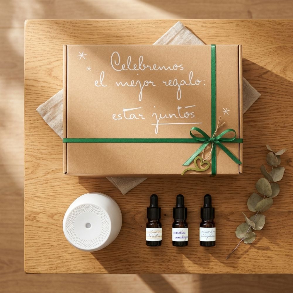 Vista cenital del cofre regalo original de D'Arome con difusor Sira blanco, trío de mini esencias LoeS y caja kraft con lazo verde "Celebremos el mejor regalo: estar juntos" sobre mesa de madera con eucalipto – D'Arome
