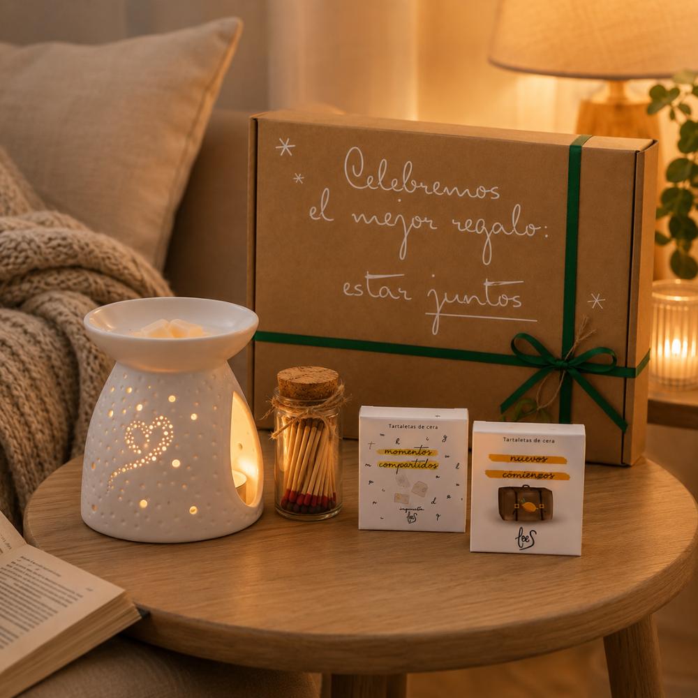 Quemador corazón de cerámica encendido con luz cálida filtrándose por los corazones perforados, junto a tartaletas de cera Momentos Compartidos y Nuevos Comienzos de LoeS, cerillas y cofre regalo D'Arome en mesita de salón – D'Arome