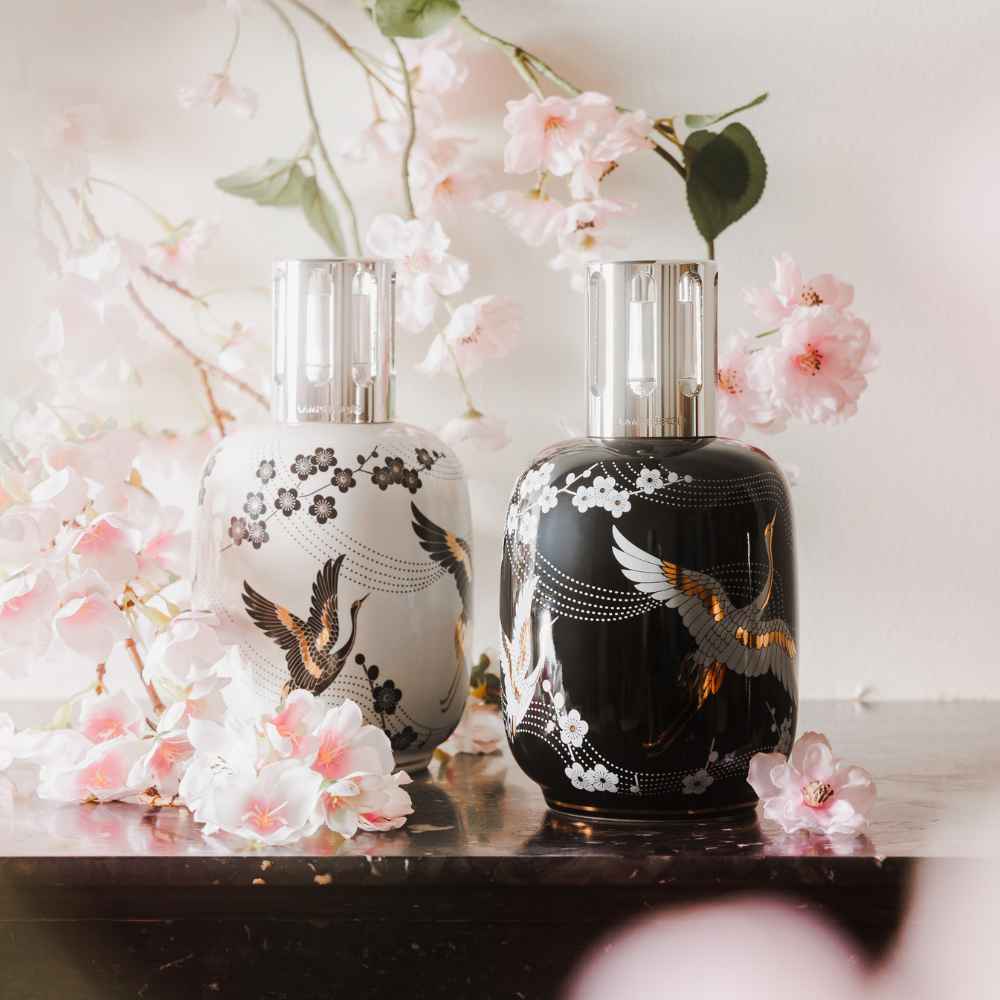 Colección Sakura Maison Berger en blanco y negro rodeada de flores de cerezo sobre superficie de mármol oscuro – D'Arome
