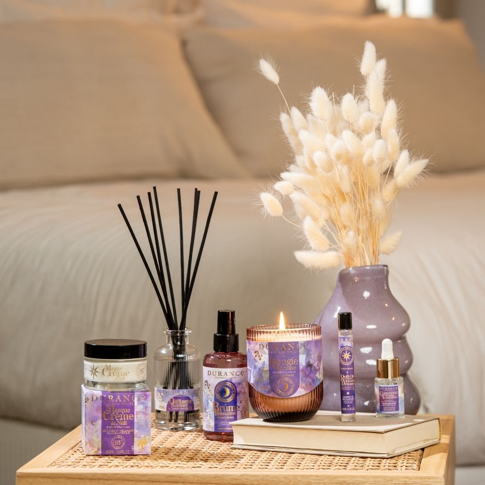 Composición completa de la Colección Serenidad Durance con mascarilla de noche, mikado, bruma de almohada, vela, sérum y roll-on sobre mesita de mimbre – D'Arome