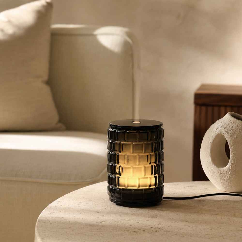 Difusor eléctrico celebration de cristal ahumado texturizado Maison Berger encendido sobre mesa auxiliar en un salón – D'Arome