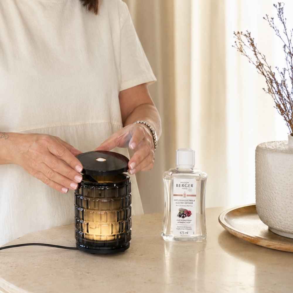 Mujer utilizando el difusor eléctrico celebration de cristal Maison Berger junto a la recarga Oud Hipnótico de 475 ml – D'Arome