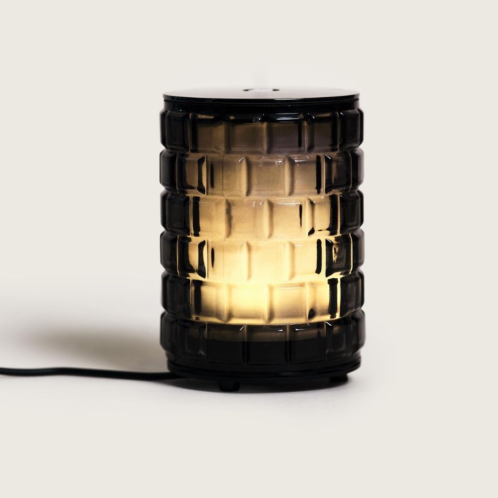 Vista completa del difusor eléctrico Celebration Maison Berger encendido con cristal negro tallado iluminado por dentro con luz ámbar y cable de alimentación – D'Arome