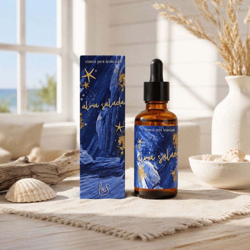 Esencia para brumizador Alma Salada de LoeS con caja azul marino y estrellas doradas junto a conchas, madera de mar y espigas en ambiente costero con vista al mar – D'Arome