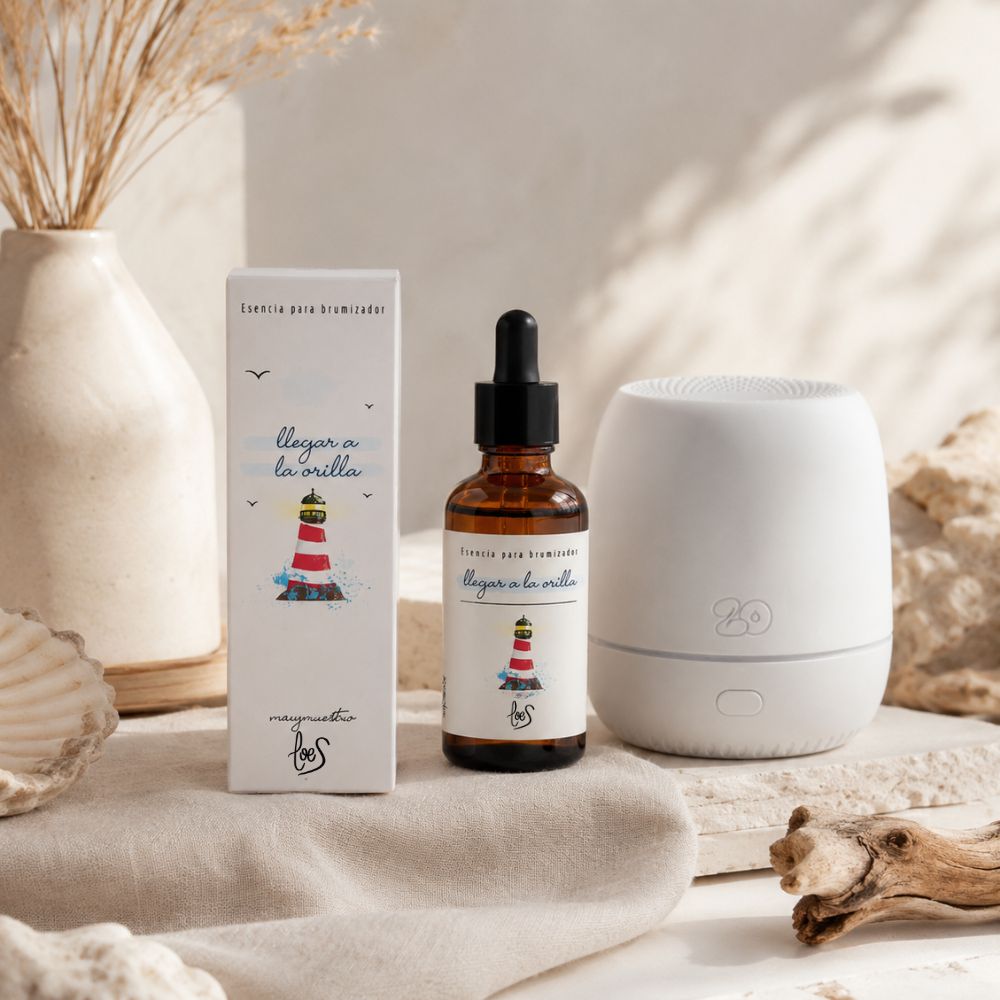 Esencia para difusor de aromas "Llegar a la orilla" de LoeS con difusor eléctrico blanco, ambientada con concha de mar, madera deriva y jarrón con pampas, evocando la calma de la orilla – D'Arome