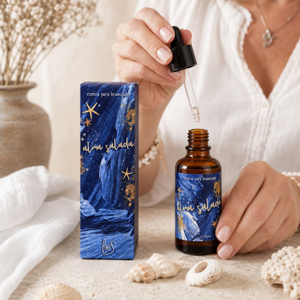 Detalle de la esencia para difusor de aromas Alma Salada de LoeS mostrando la pipeta cuentagotas con gotas de esencia, junto a caja azul con estrellas doradas, conchas marinas y corales – D'Arome