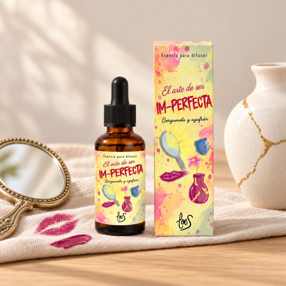 Esencia para difusor Im-Perfecta de LoeS junto a un espejo de mano dorado y marcas de pintalabios sobre un textil de lino – D'Arome