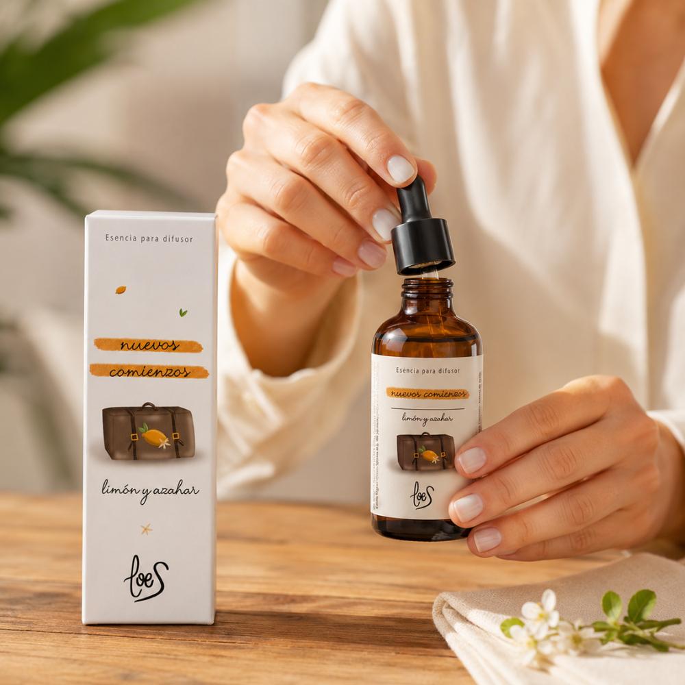 Manos con uñas blancas abriendo la pipeta de la esencia para difusor Nuevos Comienzos LoeS limón y azahar con caja y flores de azahar – D'Arome