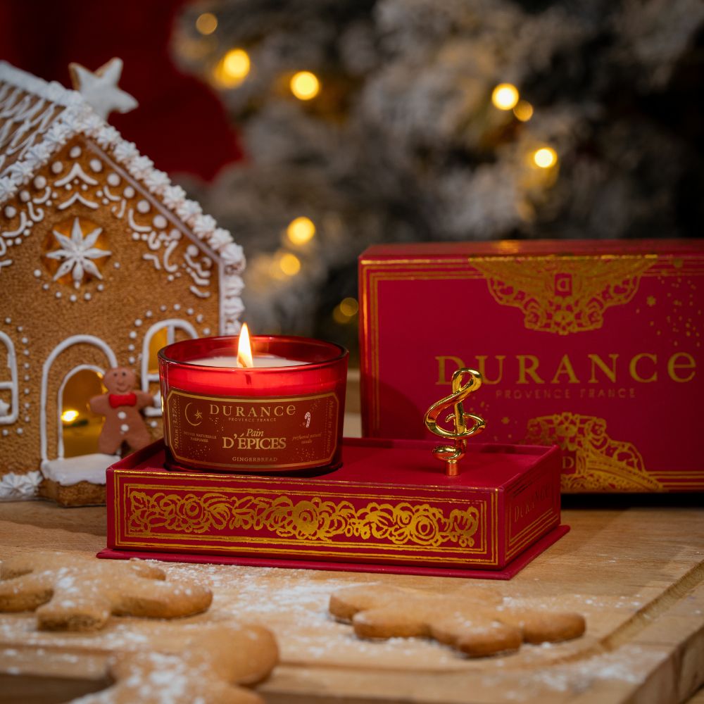 Vela Pan de Especias 90gr de Durance encendida sobre su caja de música Coffret Musical, con casita de jengibre y galletas de mantequilla en primer plano – D'Arome
