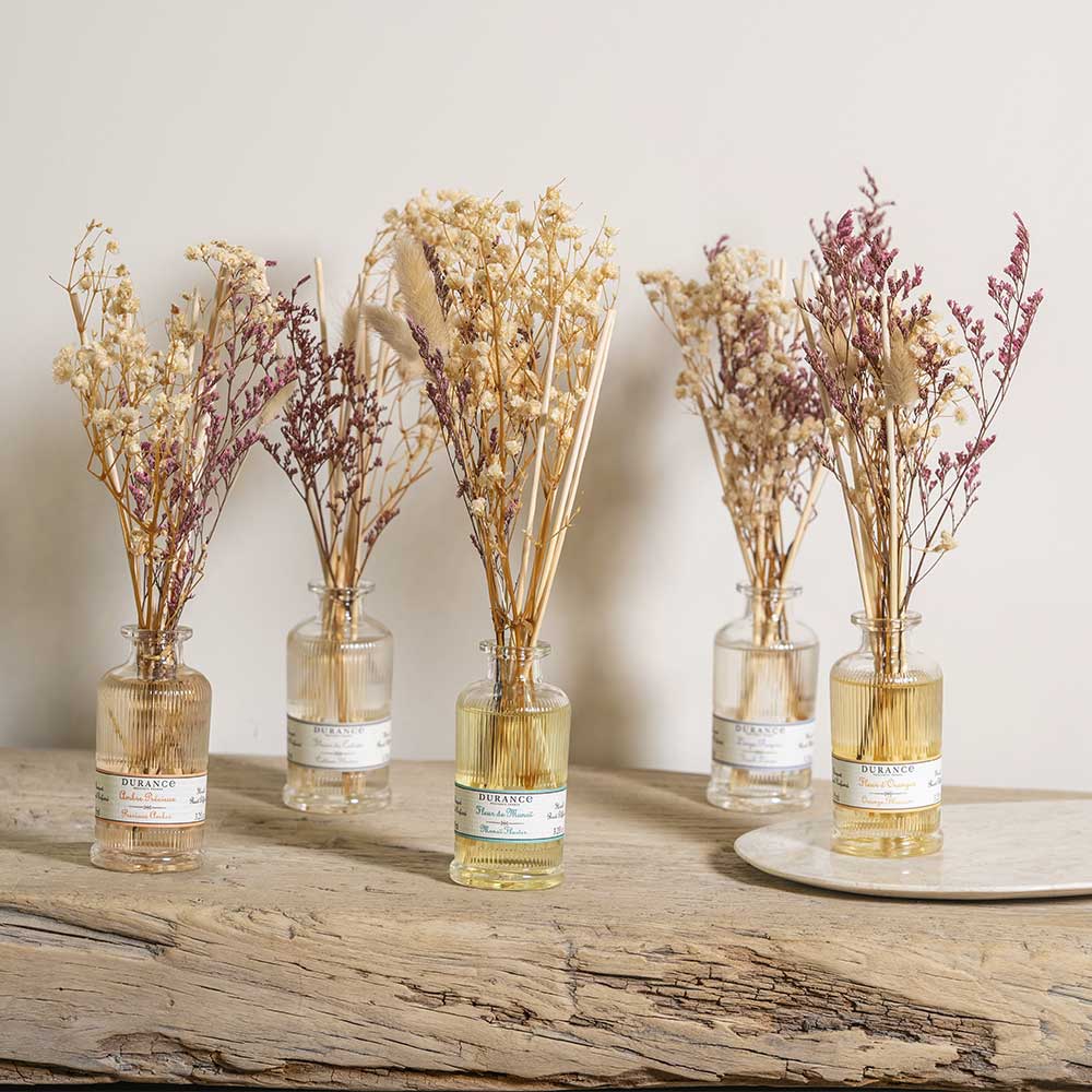 Colección de ambientadores mikado con flores secas naturales de Durance en diferentes aromas, colocados sobre un elegante expositor de mármol y dorado.