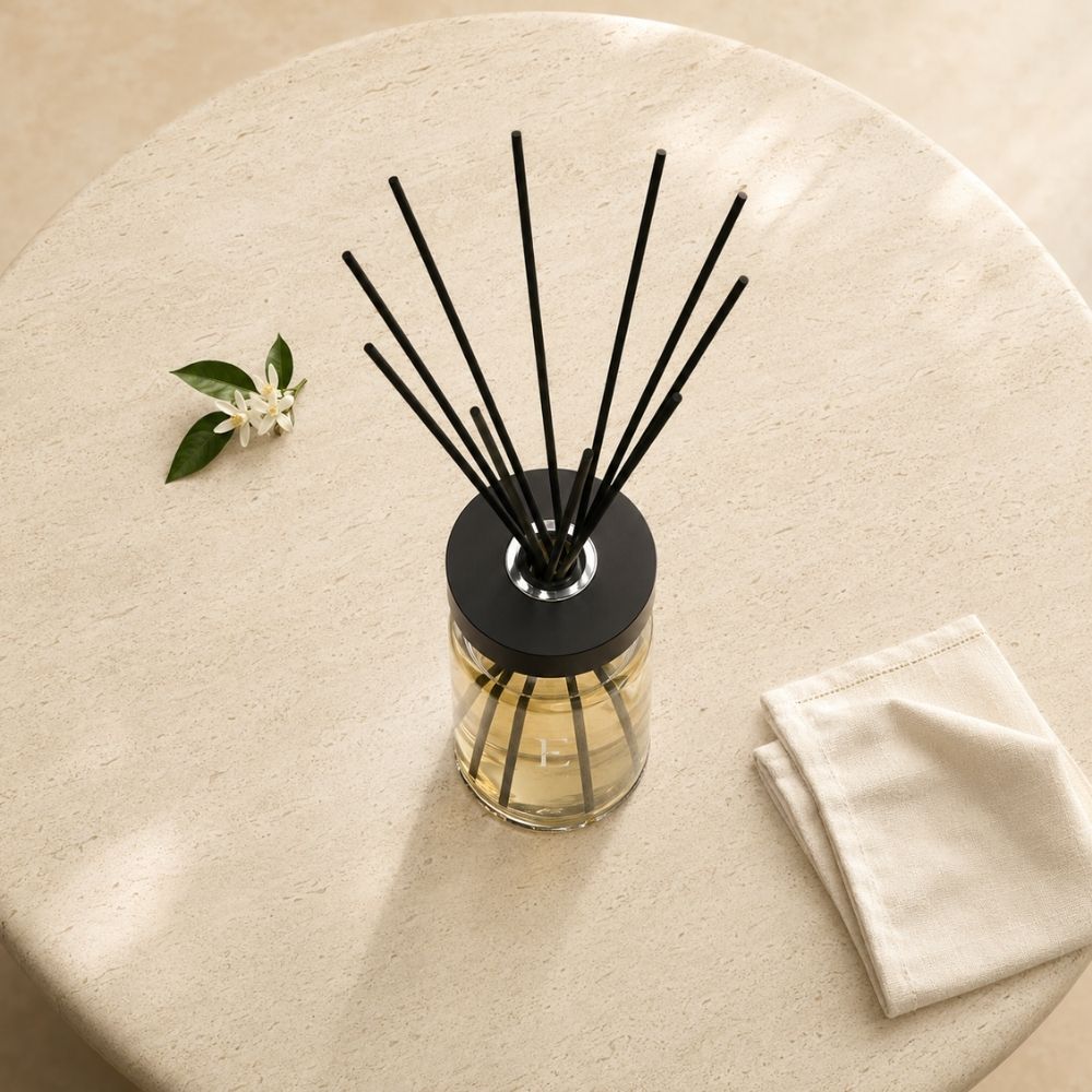 Composición cenital del difusor Néroli de Esteban Paris sobre una mesa redonda de piedra, con flor de azahar y servilleta de lino doblada – D'Arome
