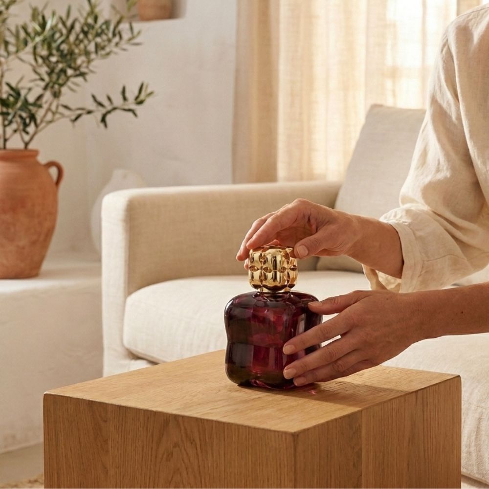 Mujer colocando la Lámpara catalítica Cosy Granate Maison Berger en salón luminoso
