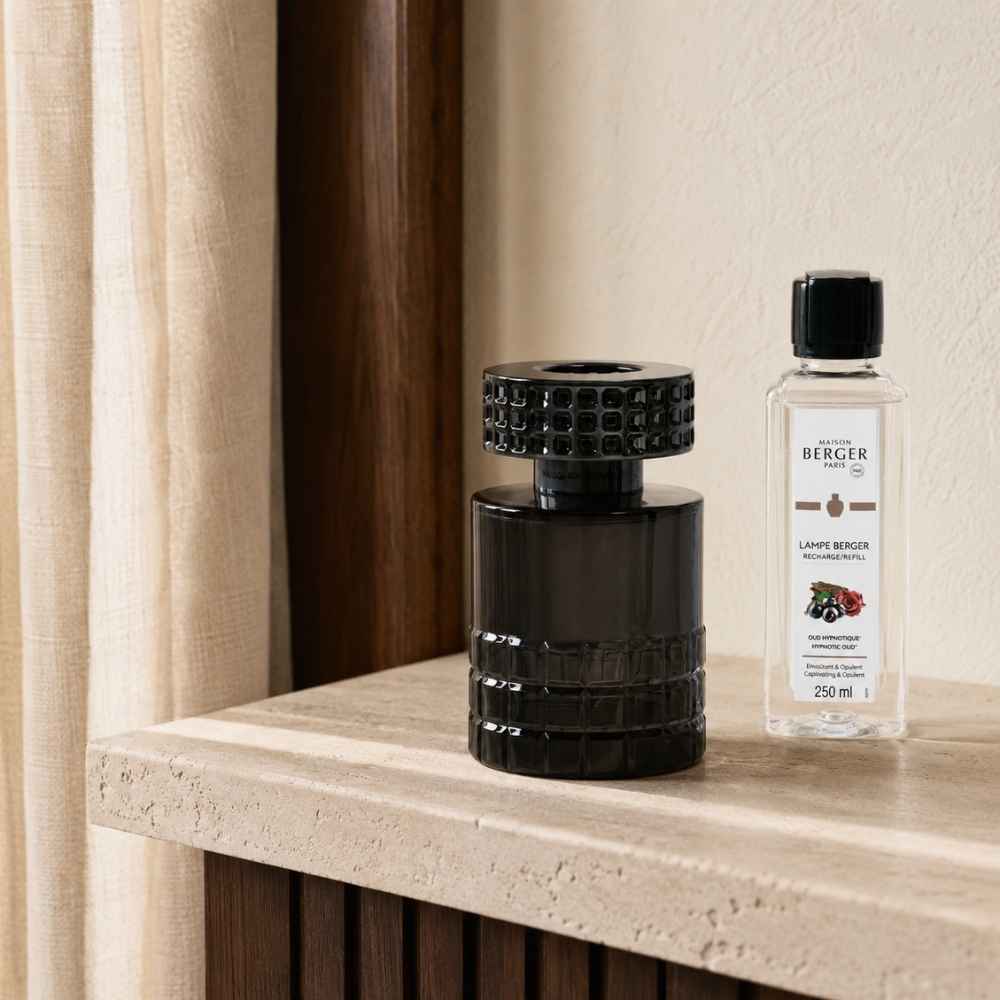 Lámpara catalítica Celebration Negra Maison Berger con montura gunmetal junto al recambio Oud Hypnotique 250ml sobre balda de piedra natural – D'Arome
