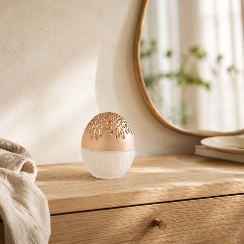 Lámpara catalítica Luka Escarchada Maison Berger con cuerpo de cristal esmerilado y capuchón troquelado en oro rosa sobre cómoda de madera – D'Arome