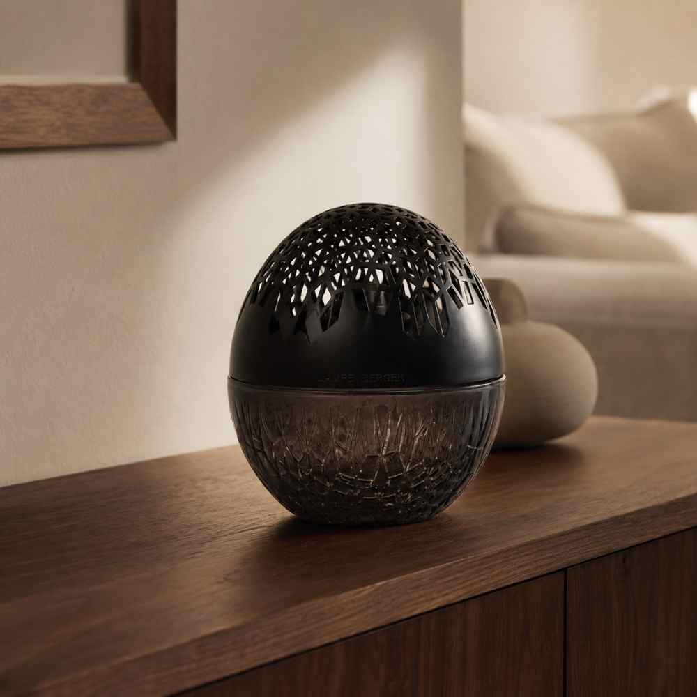 Lámpara catalítica Luka Negra Maison Berger con cuerpo de cristal ahumado tallado y capuchón negro calado sobre mueble de madera – D'Arome