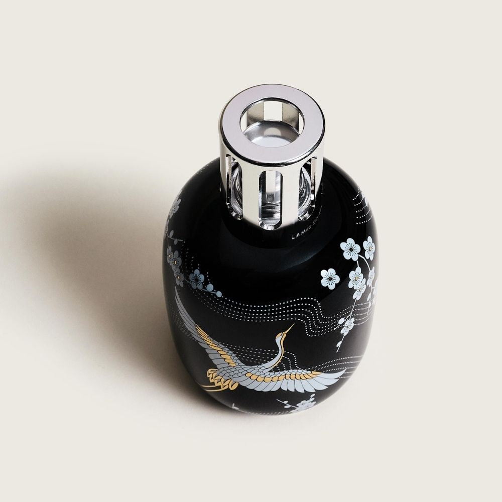 Vista cenital de la lámpara catalítica Sakura Negra Maison Berger con ilustración japonesa de flor de cerezo blanca y grulla en tonos plata y oro sobre cerámica negra – D'Arome