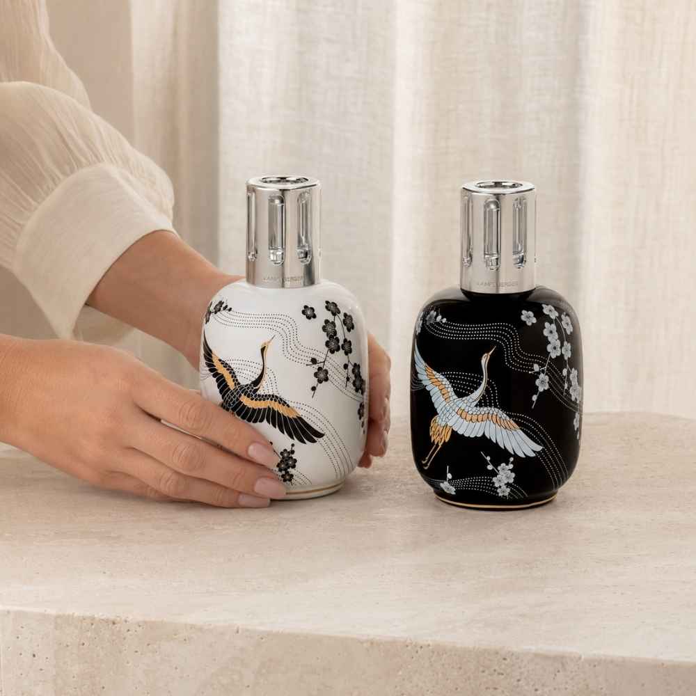 Detalle de manos colocando las lámparas Sakura Blanca y Negra Maison Berger sobre superficie de piedra clara – D'Arome