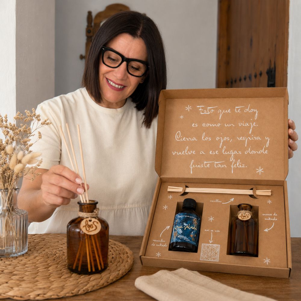 Mari Carmen, CEO y experta en aromas de D'Arome, colocando las varillas de ratán en el frasco mikado recargado con aroma Alma Salada de LoeS, cofre regalo de verano al fondo – D'Arome