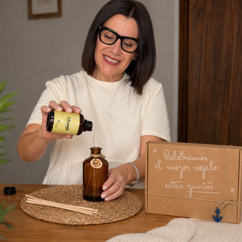Mari Carmen, CEO y experta en aromas de D'Arome, rellenando el frasco mikado de cristal ámbar con el recambio Citronela perfumado de LoeS, cofre regalo de verano al fondo – D'Arome