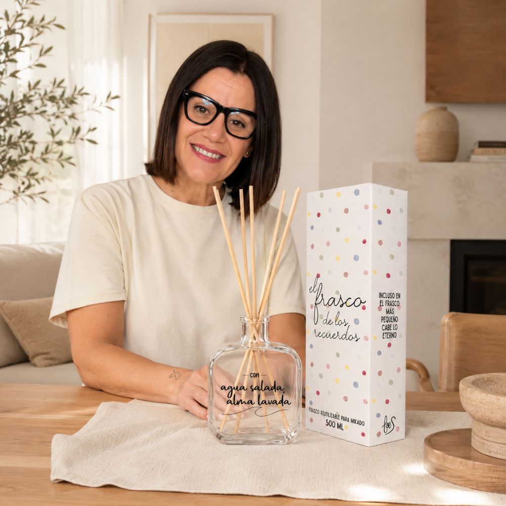 Mari Carmen, CEO y experta en aromas de D'Arome, sonriendo junto al frasco mikado reutilizable Agua Salada Alma Lavada de LoeS 500ml en un salón con chimenea – D'Arome