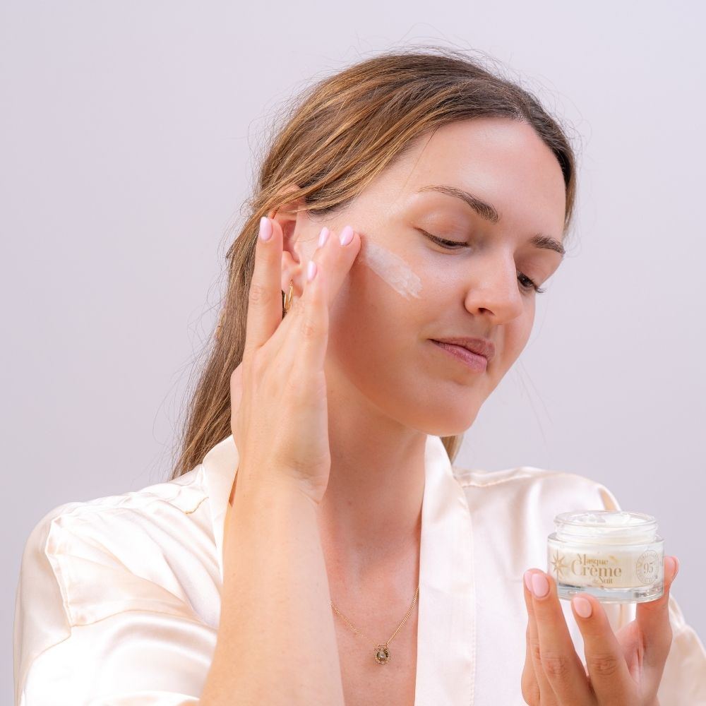 Mujer aplicando con los dedos la mascarilla crema de noche en la cara Colección Serenidad Durance frente al espejo antes de dormir – D'Arome