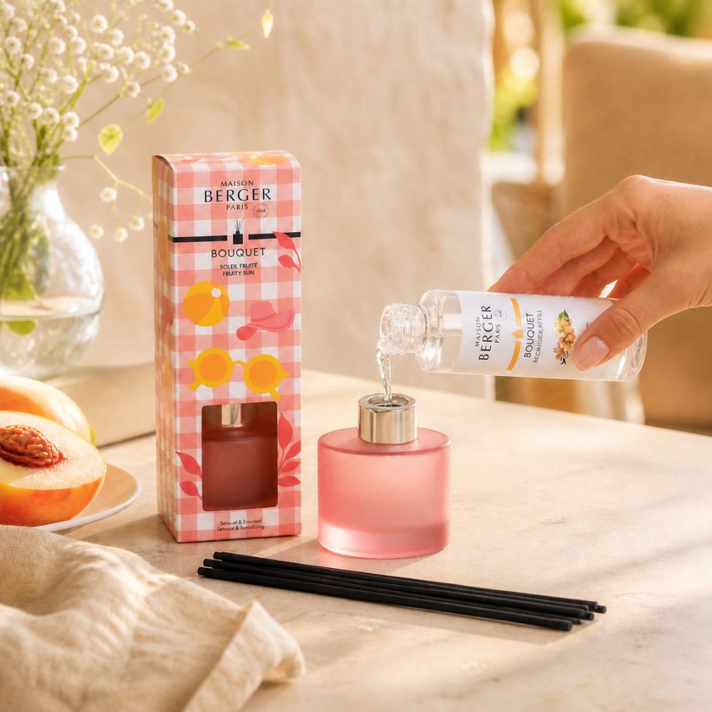 Mujer vertiendo aroma Soleil Fruité en Mini Mikado Rosa Escarchado Maison Berger en cocina con melocotones