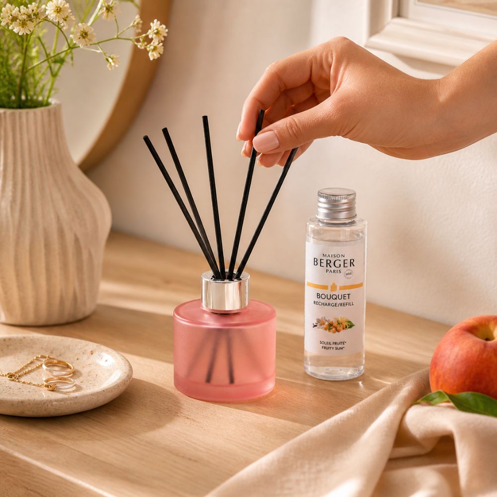 Mujer colocando varillas en Mini Mikado Rosa Escarchado Maison Berger sobre mesita de noche