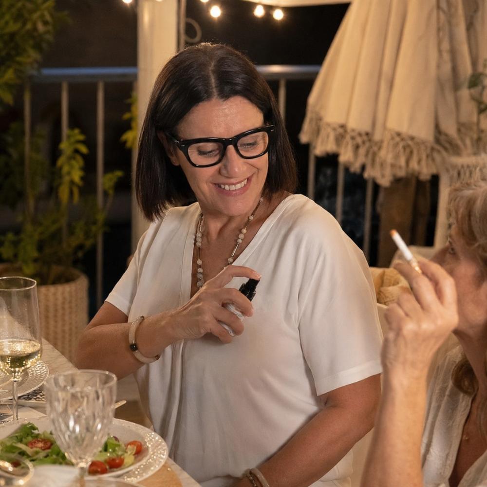 Mari Carmen, CEO y experta en aromas de D'Arome, aplica el mini spray textil Nuevos Comienzos de LoeS sobre su ropa durante cena en terraza para eliminar olor a tabaco y comida – D'Arome