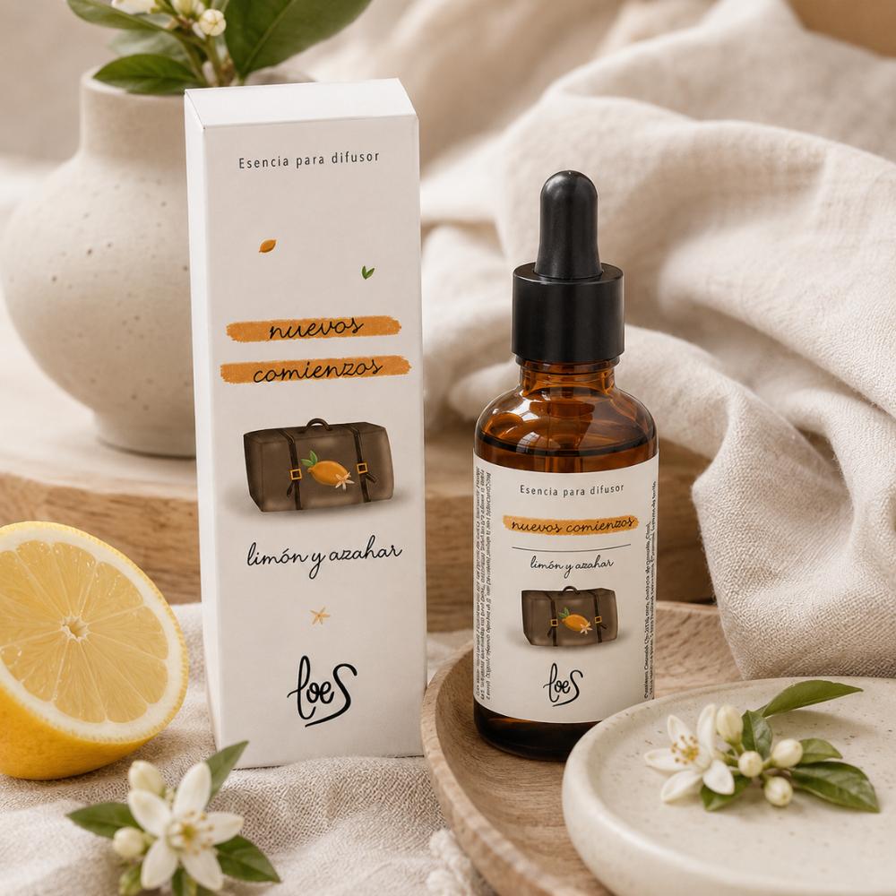Esencia para difusor Nuevos Comienzos LoeS aroma limón y azahar, frasco con pipeta y caja sobre bandeja de madera con limón fresco y flores de azahar – D'Arome