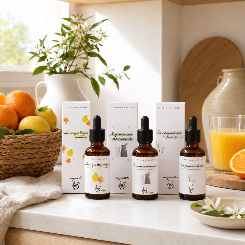 Pack tres esencias cítricas LoeS junto a cesta de naranjas y limones, vaso de zumo natural y ramo de azahar en cocina luminosa – D'Arome