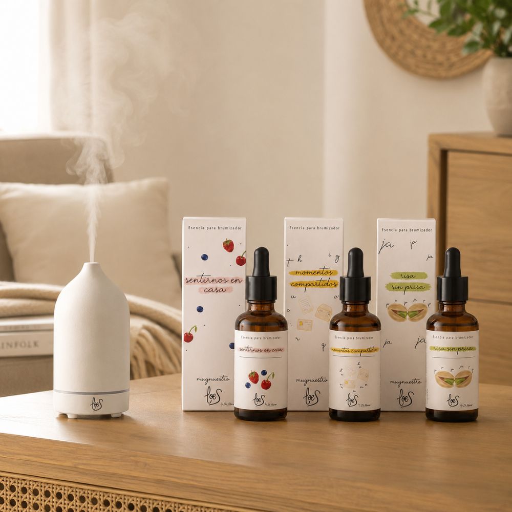 Pack de aromas dulces LoeS junto al difusor de cerámica blanca LoeS encendido sobre cómoda de salón con cojines y planta, ambiente cozy – D'Arome