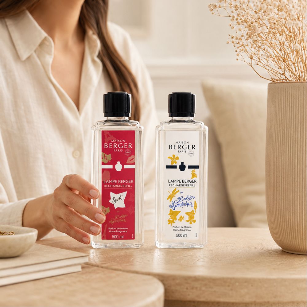 Manos colocando el pack de líquidos dulces para lámpara catalítica Maison Berger Lolita Lempicka Sweet y Lolita Lempicka 500ml sobre mesa con jarrón de flores – D'Arome